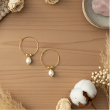 Gold hoop earrings with pearls on a wooden surface with decorative elements.