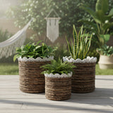 Three woven planters with plants on a wooden surface outdoors.