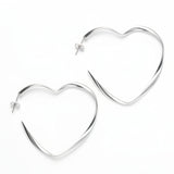 A pair of heart-shaped hoop earrings made with silver plate, laid on a dark surface.