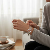 Person wearing a silver bracelet with charms in a cozy indoor setting