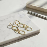 Gold chain earrings on a marble surface with a pen and notebook in the background