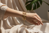 Gold chain bracelet on a white surface with a green leaf in the background