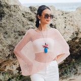 Suzie Blue Canada baby pink sheer mesh poncho worn by a model at the beach with white pants and a statement necklace.