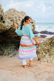 Suzie Blue Canada light blue rayon kimono with rainbow tie-dye stripes, worn over white pants on a beach.