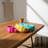 Suzie Blue Canada set of three tie dye bandanas in vibrant pink, yellow, and turquoise on a wooden table.