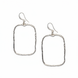 A pair of silver plate, hammered rectangular earrings laid on a light textured surface.