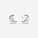 A pair of silver plate metal stud earrings shaped like a crescent moon, displayed on a dark textured surface.